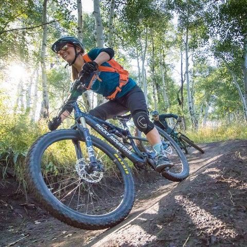 Woman mountain biking down hill with full gear on, smiling